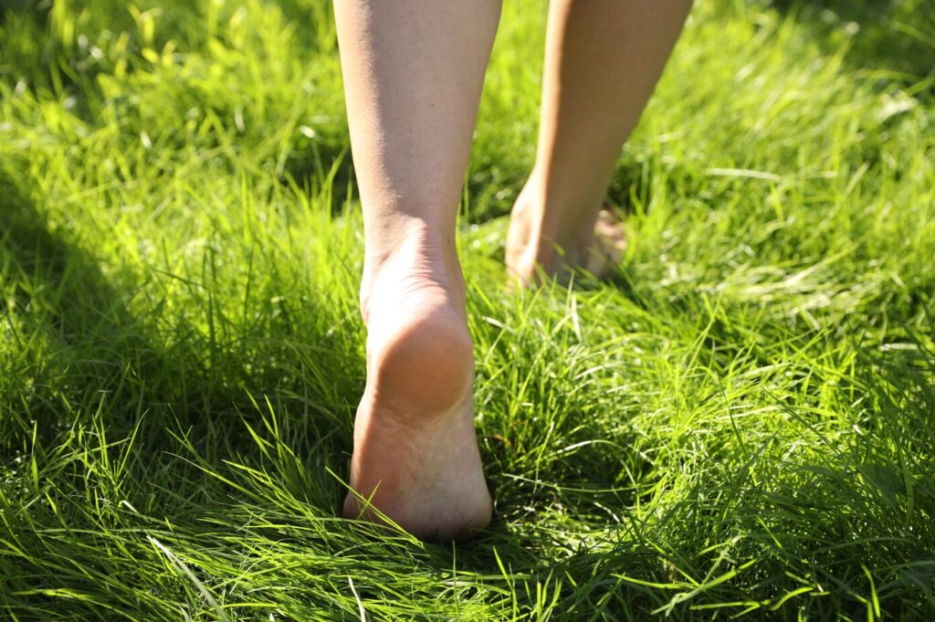 A low-angle, close-up shot of bare feet walking through lush green grass on a sunny day.