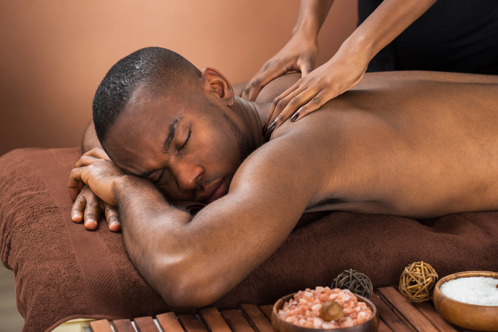 Person receiving a back massage in a spa setting, surrounded by Himalayan salt, sugar bowls, and decorative elements, evoking relaxation and wellness.