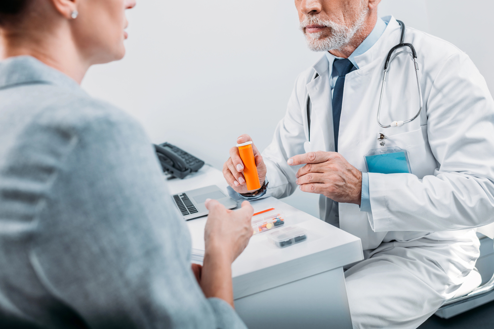 A doctor sitting at a desk, handing a bottle of pharmaceutical medicine to a patient.