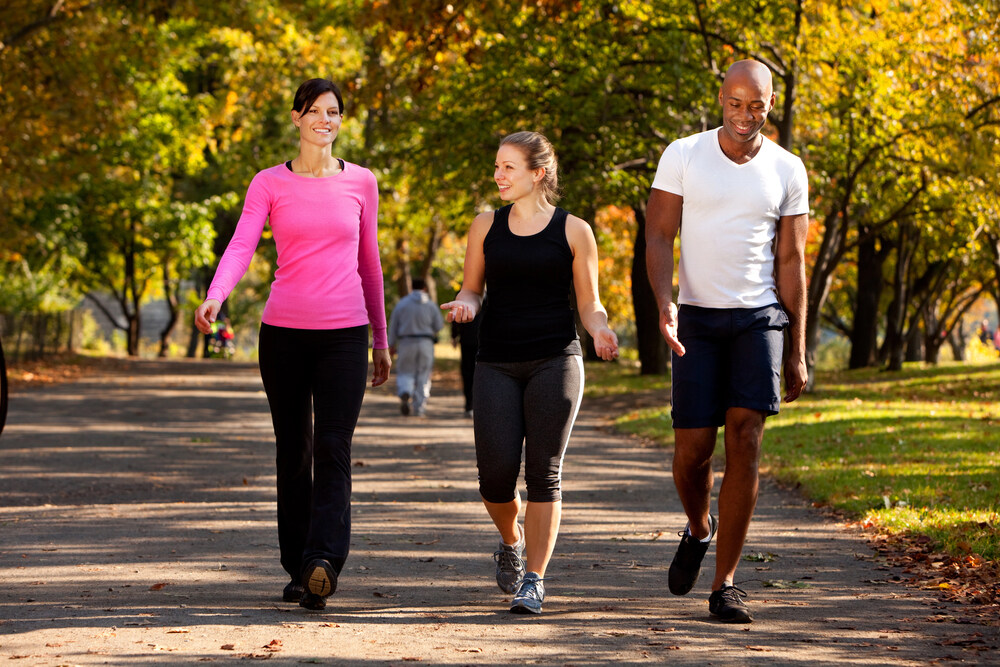 A man and two women are walking on a paved path in a park with trees in autumn.