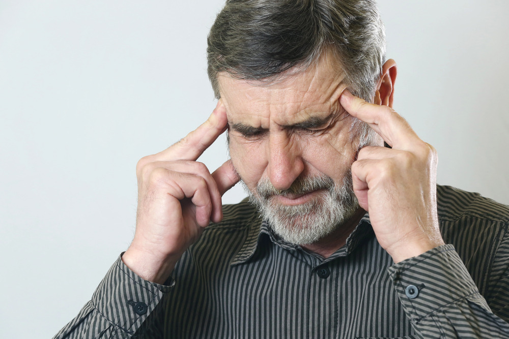Old man touching his temples with eyes closed, looking stressed and dizzy.