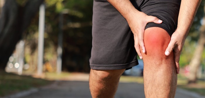Person outdoors holding their inflamed knee with both hands, visually representing joint pain or injury during physical activity.