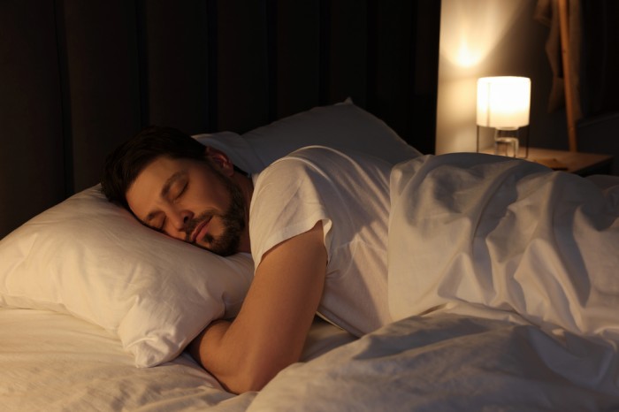 Man sleeping peacefully in bed at night with soft bedside lamp lighting the bedroom