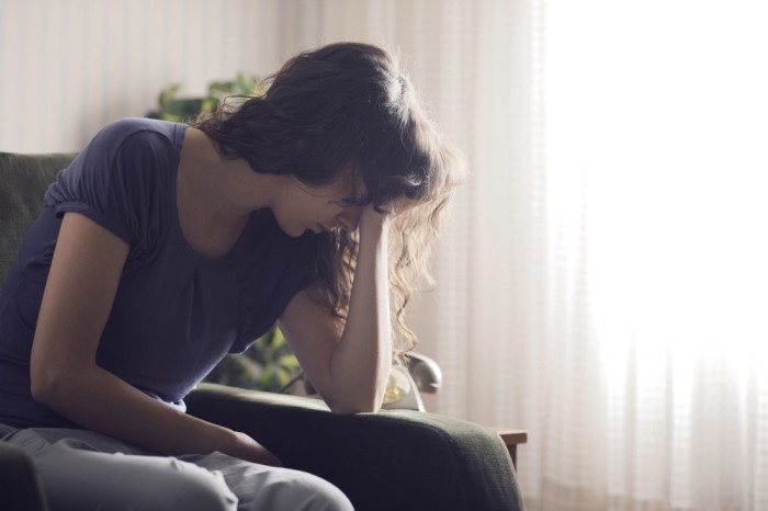 Woman sitting with head in hand, appearing fatigued or stressed in a softly lit indoor setting